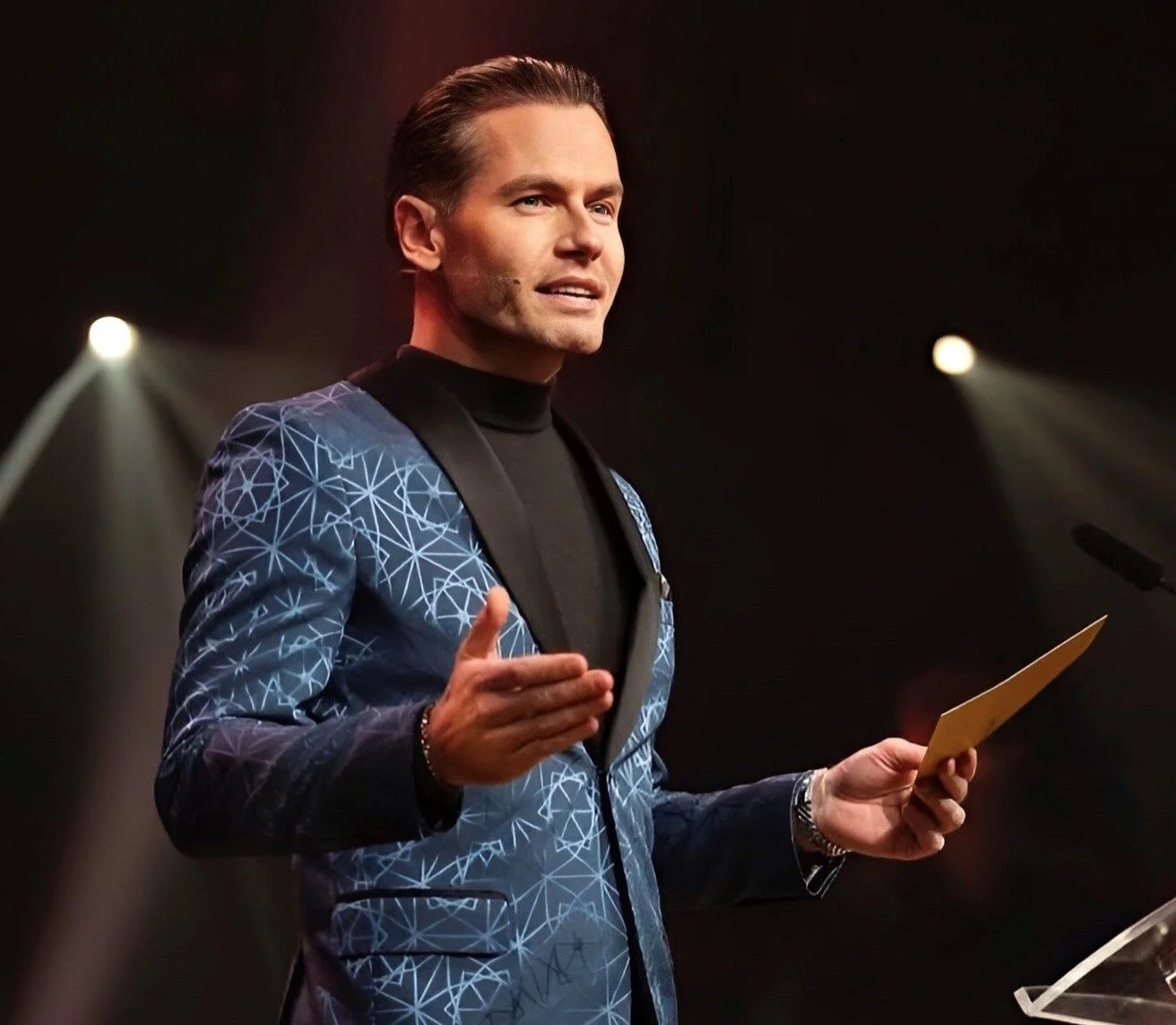 Danny Makkelie als spreker op het podium in pak met een microfoon